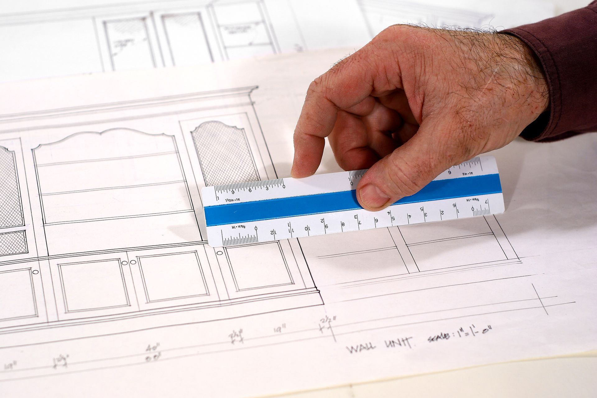 Close-up of a cabinet blueprint as a man uses a ruler to measure a side of a drawing.