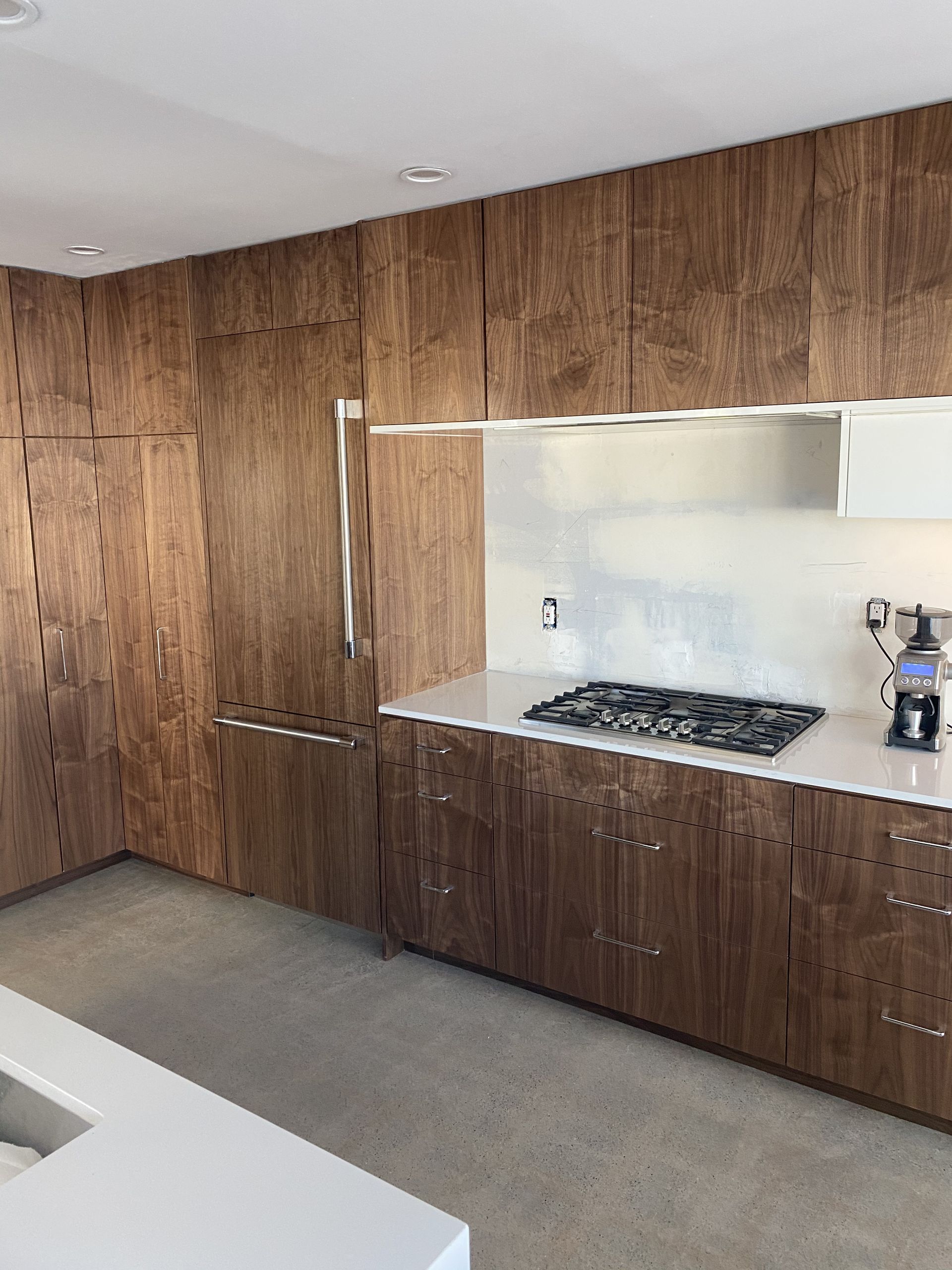 Modern kitchen with wood grain cabinets, stainless steel backsplash, and white countertops.