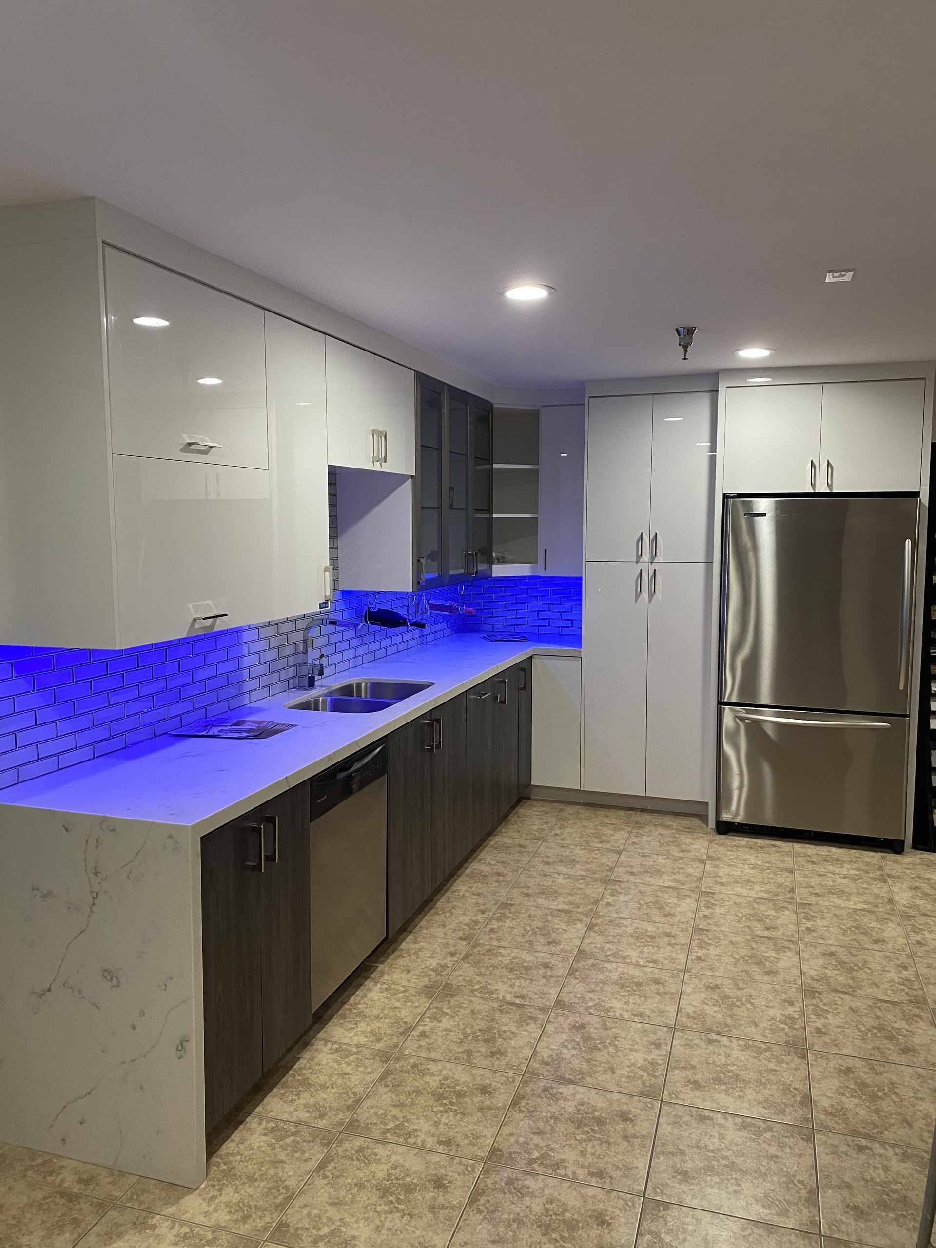 Modern kitchen with white and gray cabinets, stainless steel appliances, and blue under-cabinet lighting.