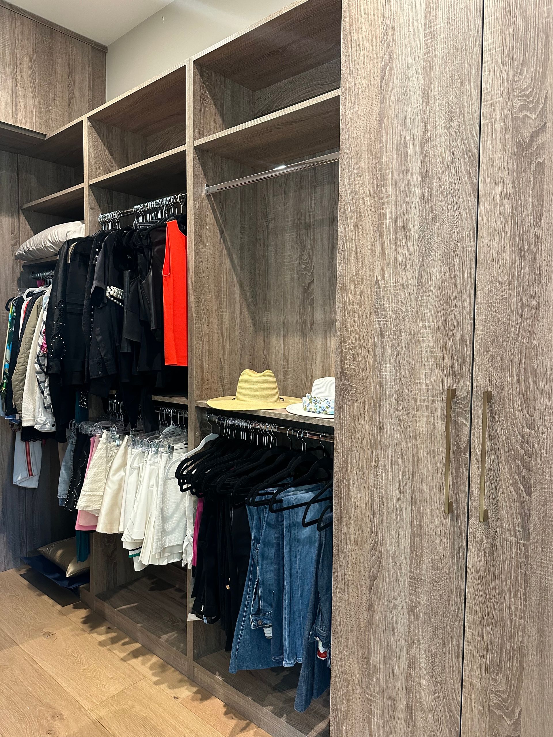 Walk-in closet with clothes hanging. Brown wood shelving and door.