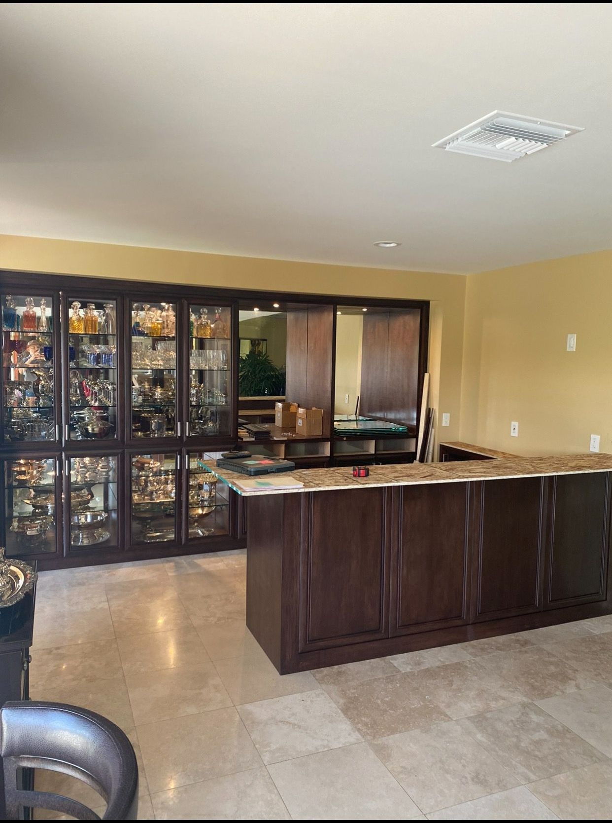 A room with a dark wood bar and cabinets, filled with glassware and decor, and a tan countertop.