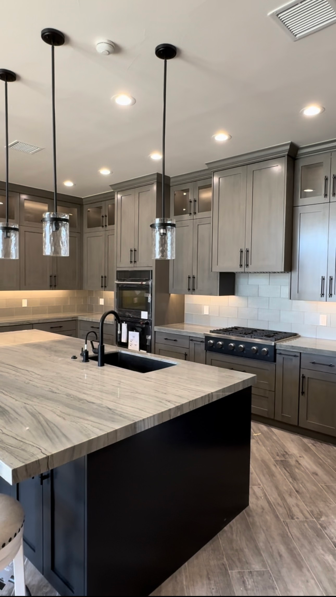 Modern kitchen with a black island, gray cabinets, and pendant lights.