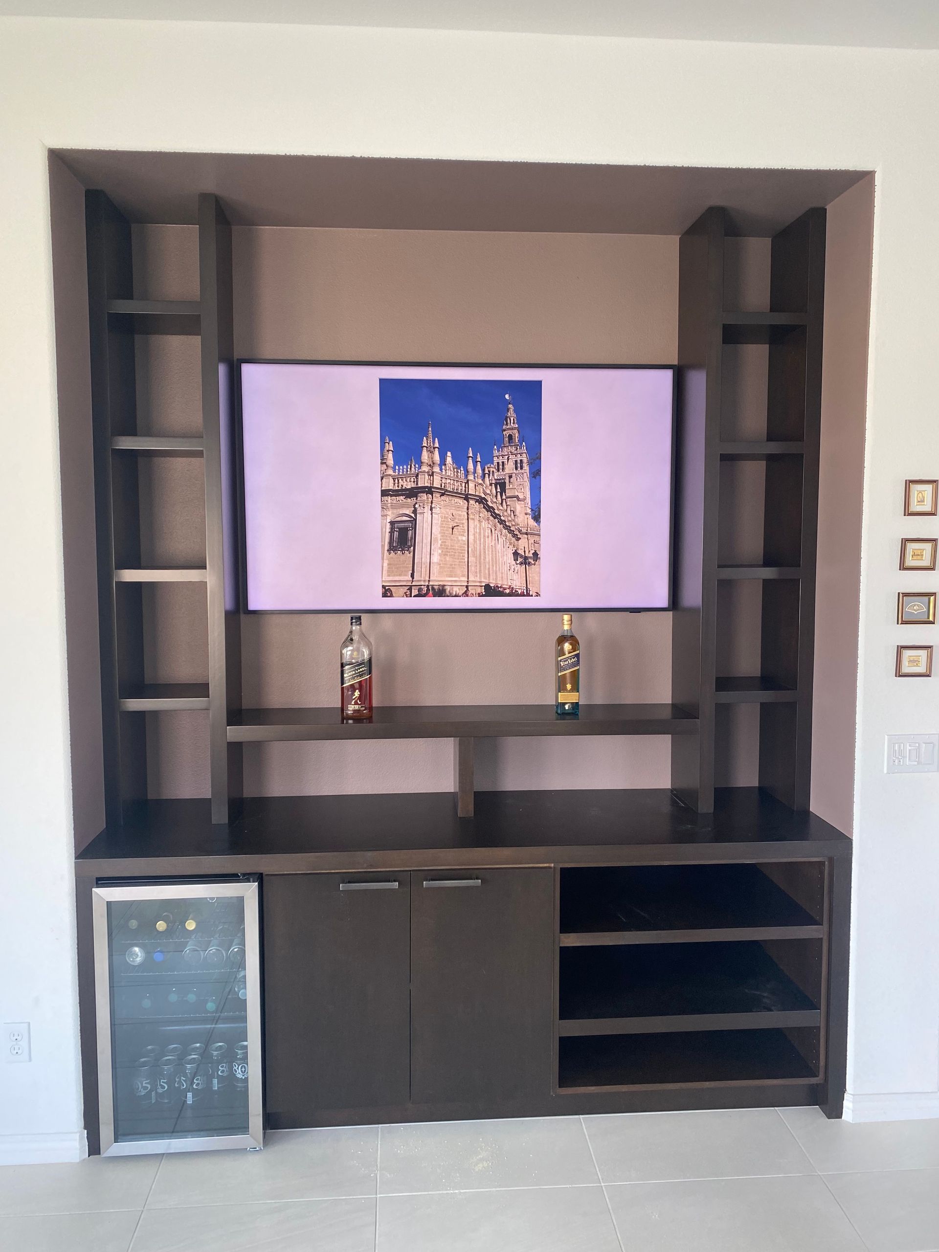 Built-in dark brown entertainment center with TV, shelves, cabinets, and a wine cooler.