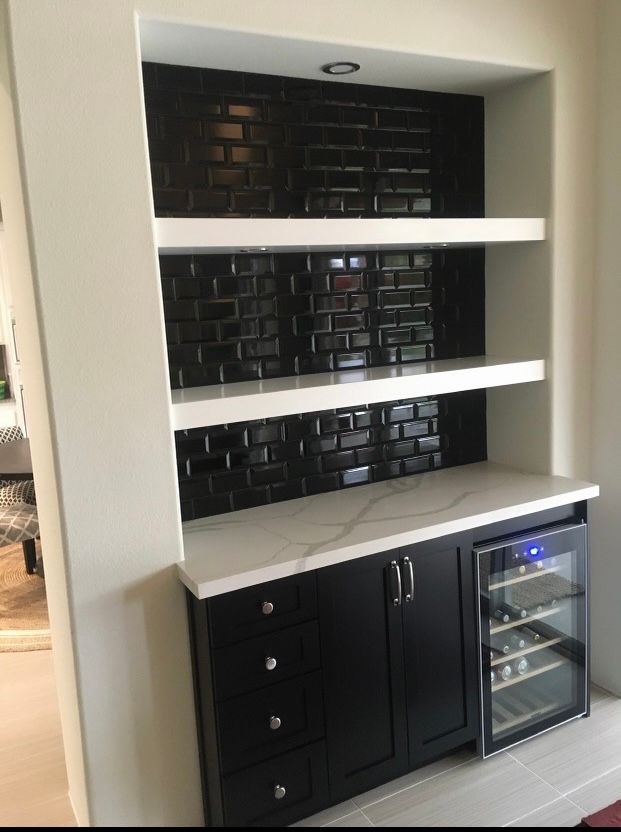 Built-in bar with black cabinets, white countertop, and shelves. Black tiled backsplash. Wine fridge.