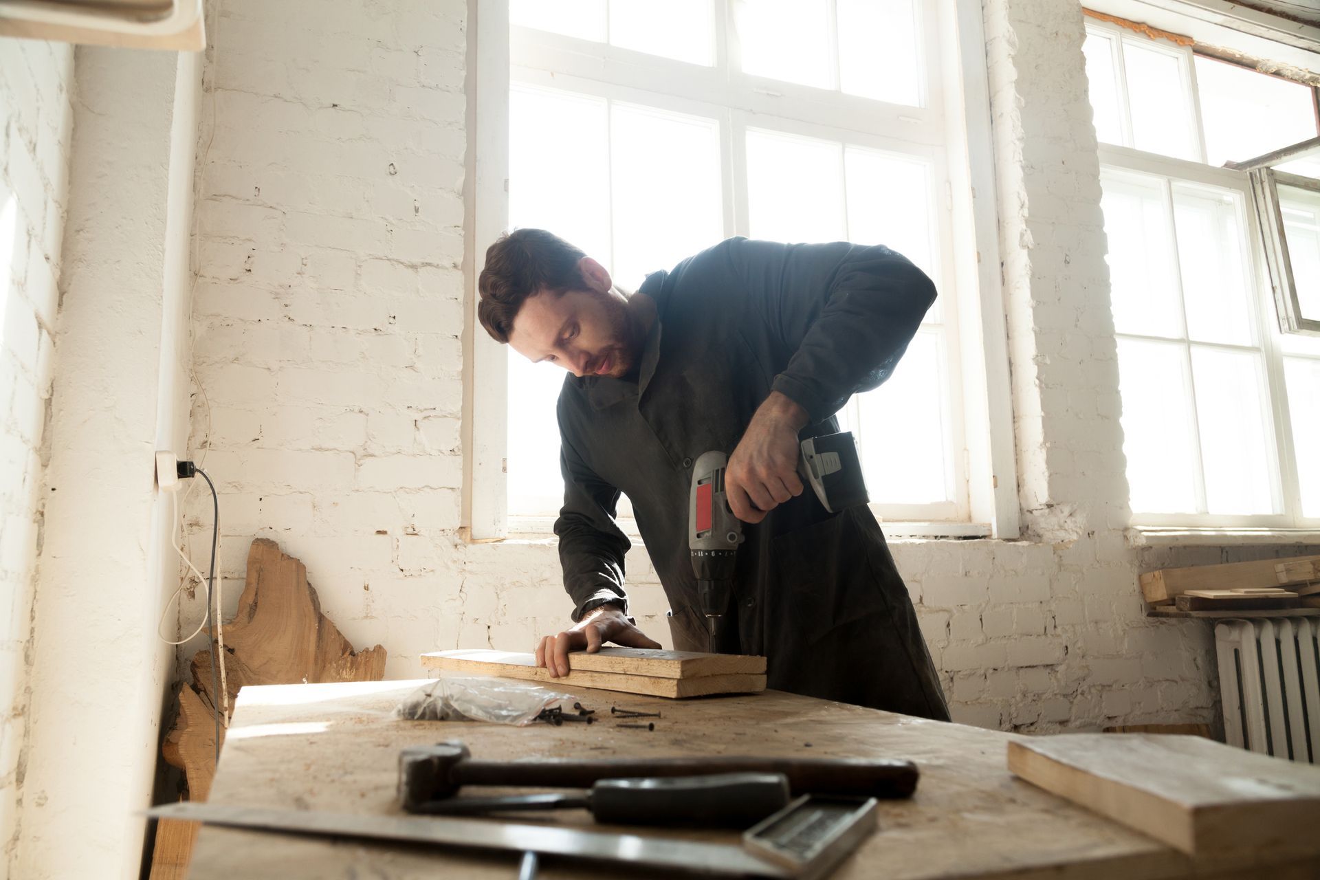A male bathroom cabinet maker works in a carpentry shop with two pieces of wood on a table.