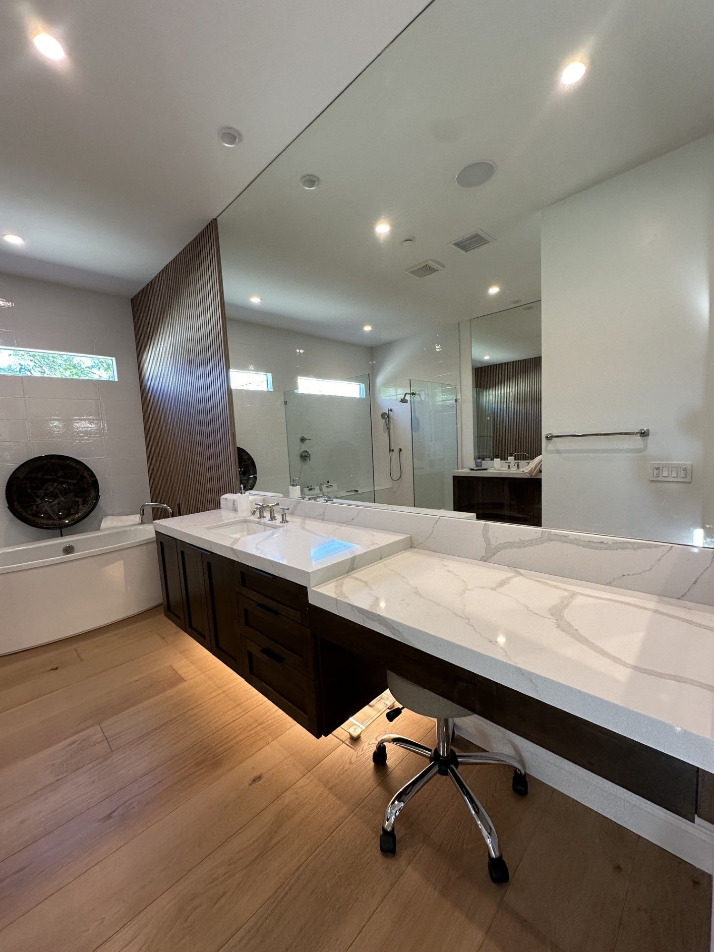 Modern bathroom with large mirror, dark vanity, white countertop, and light wood floor.