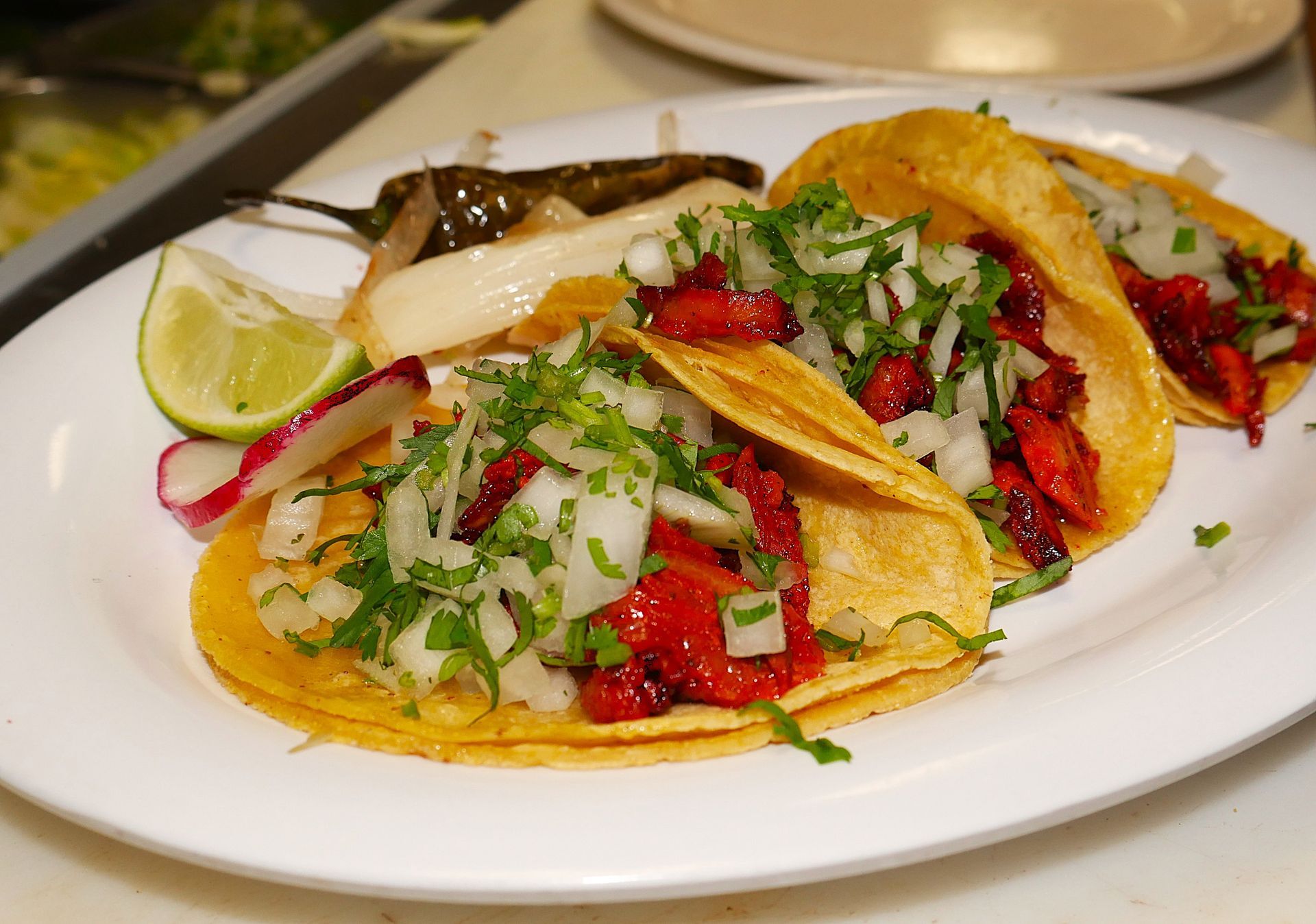 Authentic tacos al pastor with pork sliced fresh from one of Michigan's only trompo, garnished with lime, radish, & cilantro