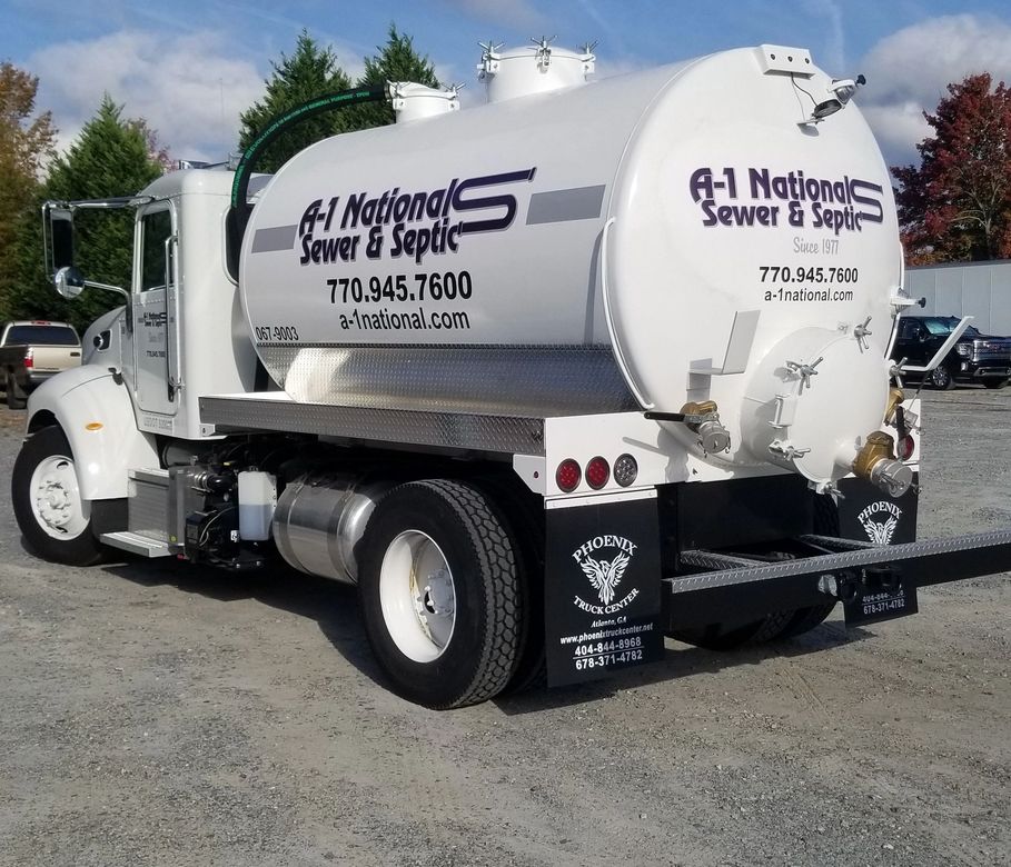 A  sewer & septic truck is parked in a gravel lot