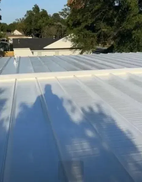 A person's shadow cast onto a white corrugated metal roof on a sunny day.