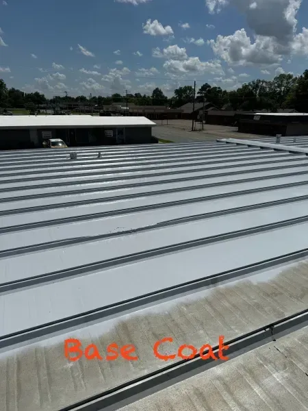 A metal roof shows a transition from an aged, weathered surface to a freshly applied white base coat coating.