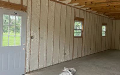 Interior of a room under construction with white spray foam insulation between wooden wall studs and a white door.