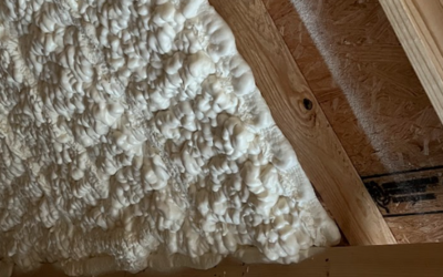 White spray foam insulation applied between wooden roof rafters in an attic space.