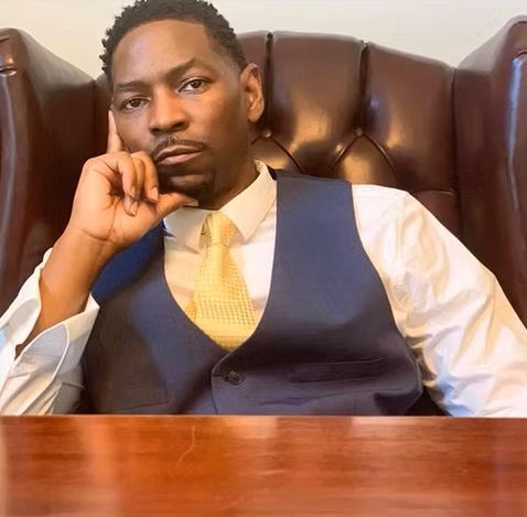 A man in a vest and tie is sitting in a chair