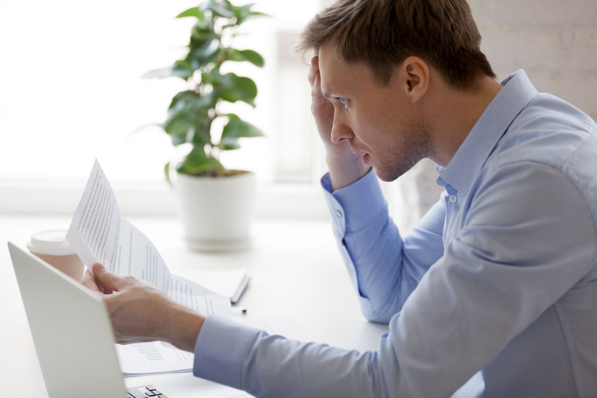 A man reading a notification from a bank about unpaid debt. Unfocused plant in the background.