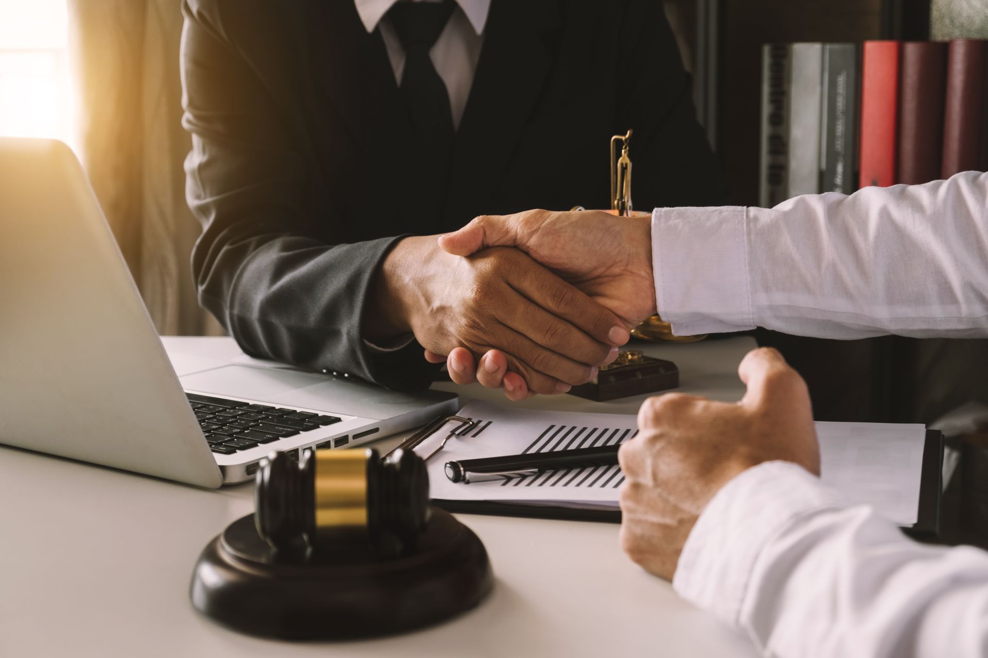 Two people shaking hands across a desk with legal documents and a gavel.
