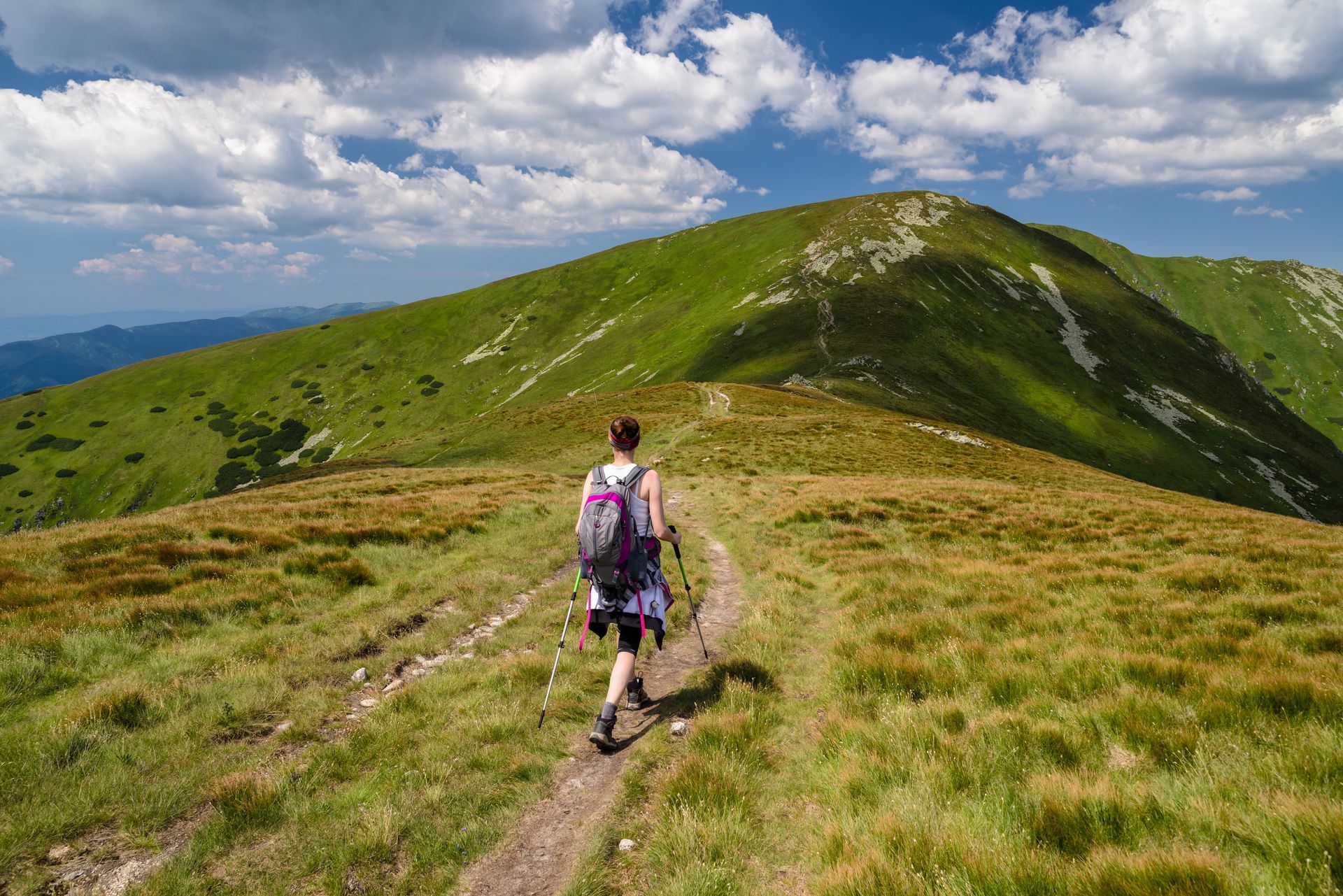 Turistka stúpa po trávnatom kopci po prašnej ceste.