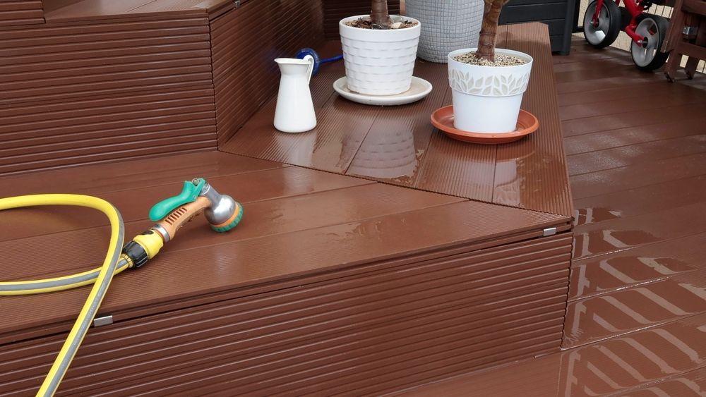 A hose is sitting on a wooden deck next to potted plants.