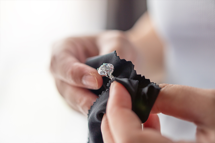 A person is cleaning a diamond ring with a black cloth.
