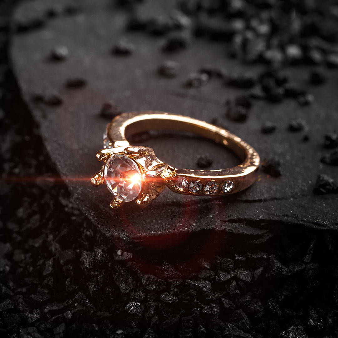 A close up of a gold ring with a diamond on a black surface.