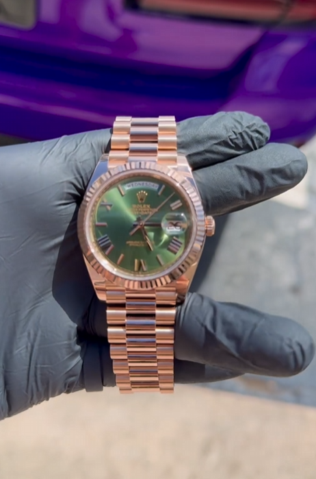 A person wearing black gloves is holding a watch with a green face.