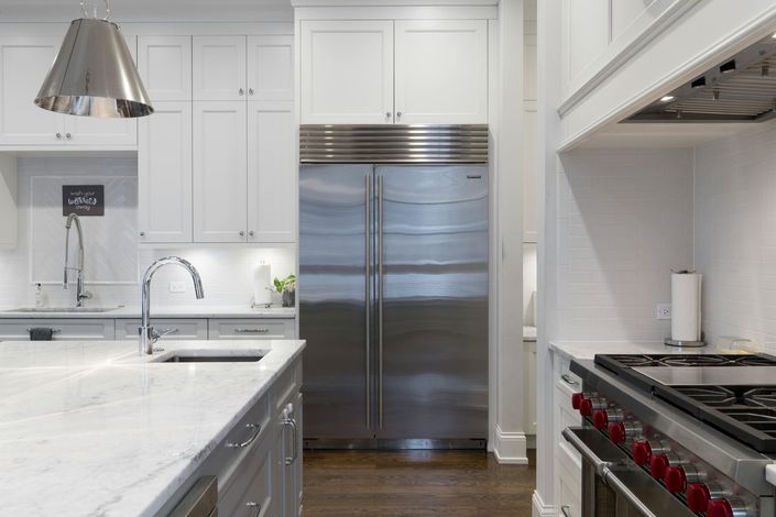 Modern white kitchen with stainless steel appliances, large fridge, sink island, and gas range in the foreground