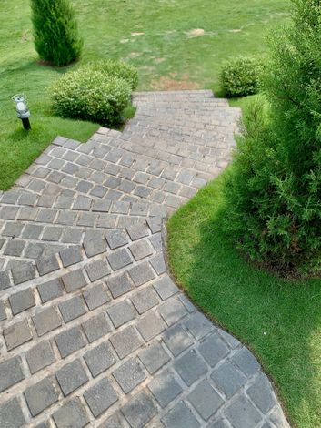 Curved stone walkway through a green lawn with trimmed shrubs and a small garden light