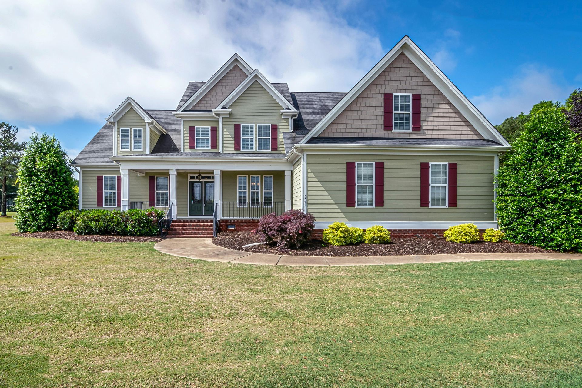 Large beige two-story suburban house with red shutters, a front porch, and a wide lawn