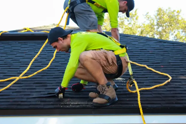 Worker kneeling on a roof, securing yellow safety ropes during rooftop maintenance.
