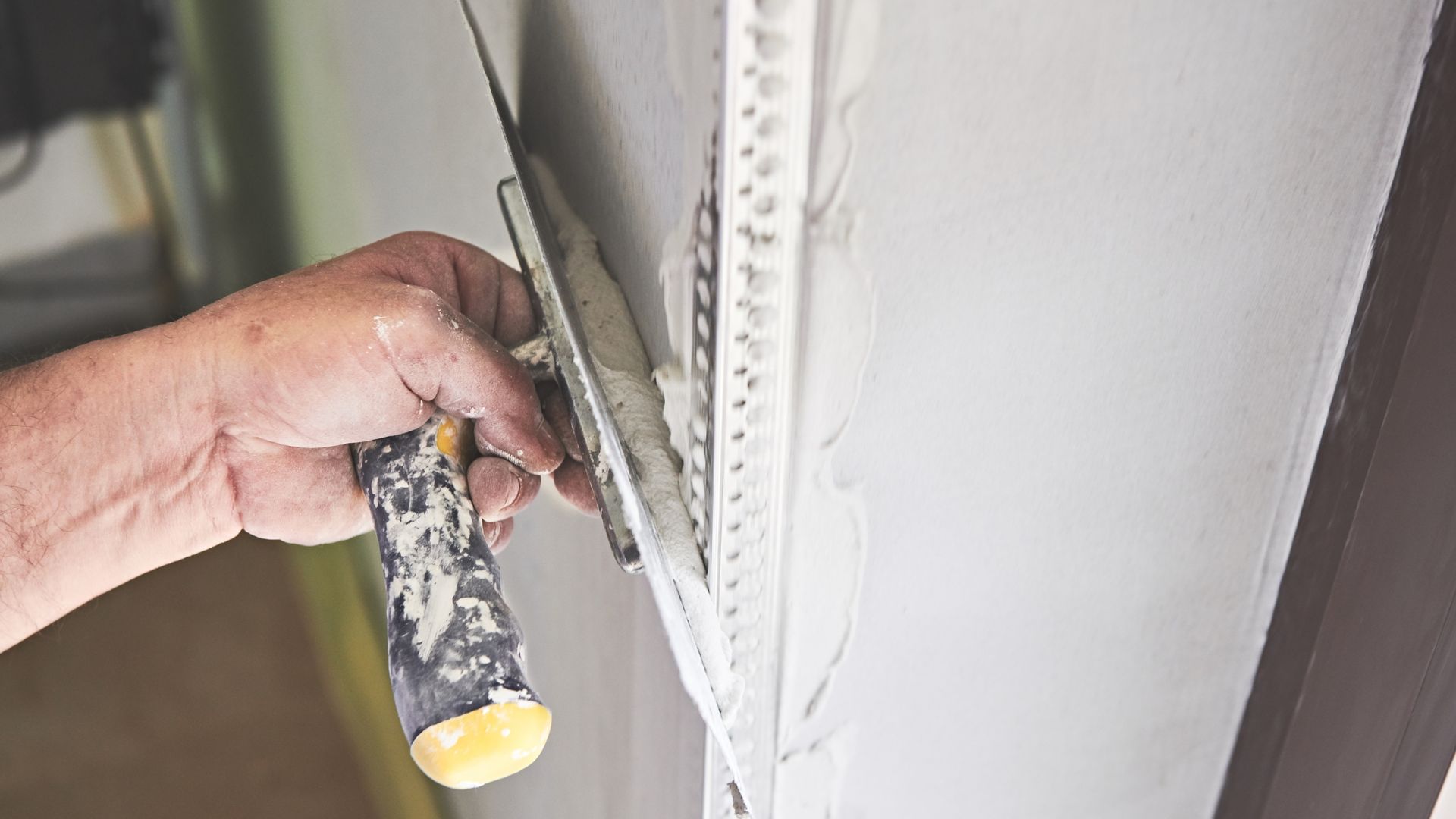 Hand holding a paintbrush painting white trim along a wall edge