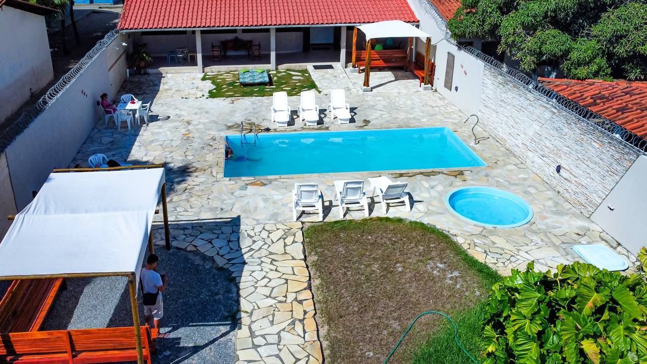 Vista aérea de uma casa com piscina. A propriedade conta com uma piscina retangular, espreguiçadeiras e uma pequena piscina redonda, cercada por um pátio de pedra.Pousada Pitagnda Prado