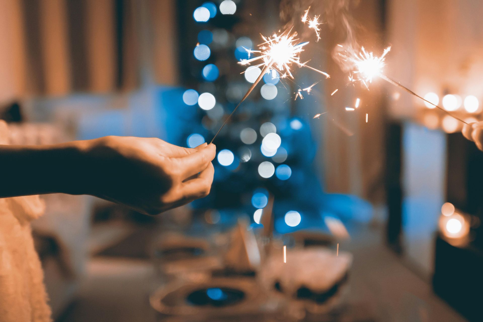 Person holding sparklers in a room with Christmas tree in the background.