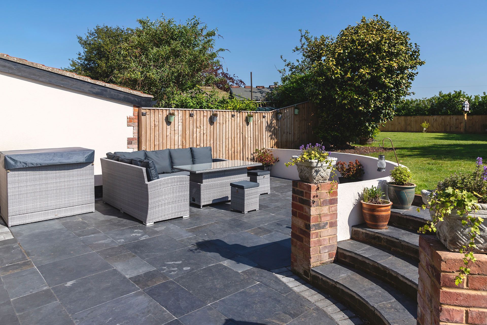 An outdoor kitchen with stone counters and a built-in grill under a wooden pergola, overlooking a wooded autumn scene.