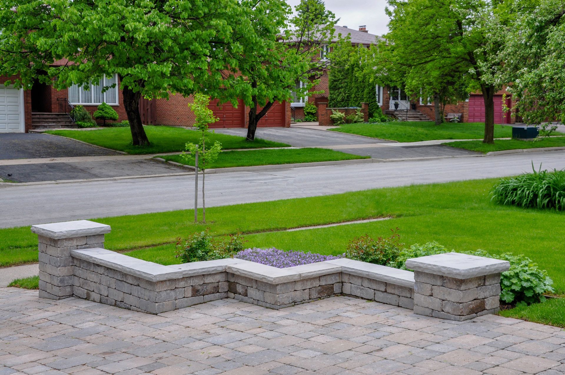 A light-grey stone seat wall with two pillars bordering a patio in a grassy residential neighborhood.