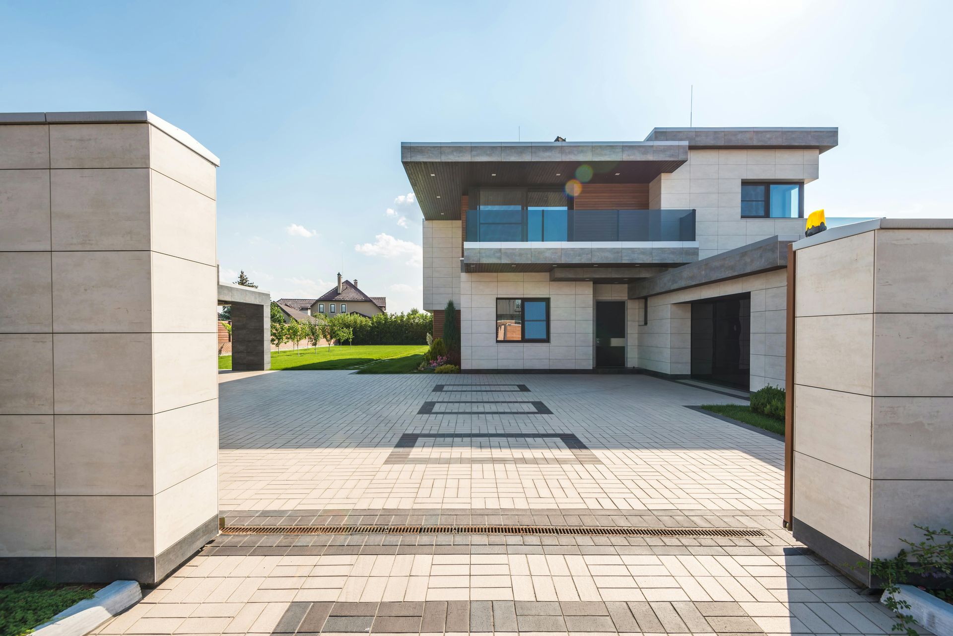 A modern house with light stone siding and a flat roof, viewed through an open stone gate leading to a paved driveway.
