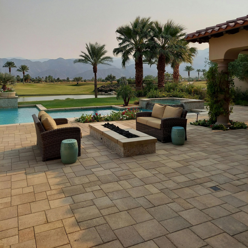 A patio with wicker chairs and a fire pit overlooking a pool, golf course, and mountains under a hazy sky.