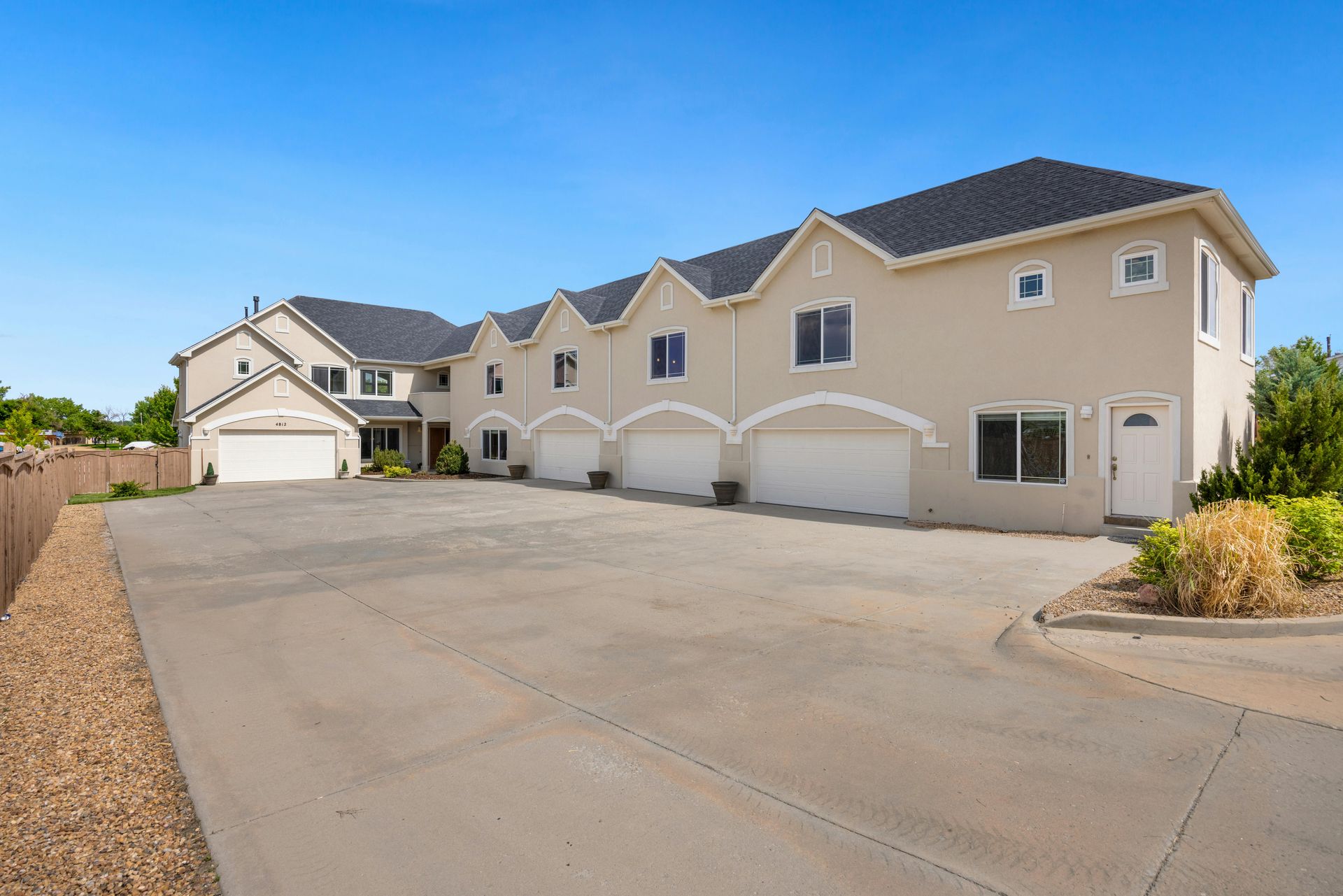 A multi-unit beige townhouse building with multiple garage doors, set against a bright blue sky.