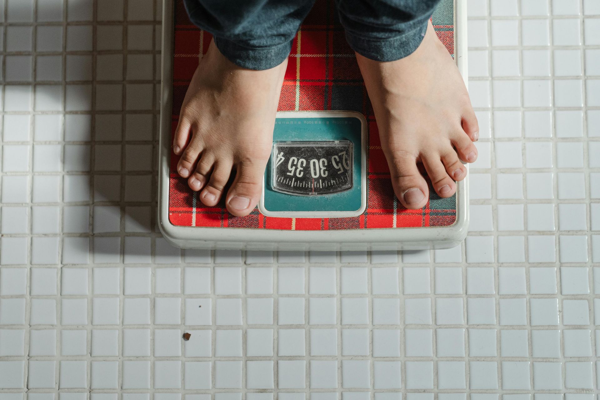 Bare feet standing on an old red and white bathroom scale. The scale reads approximately 35.