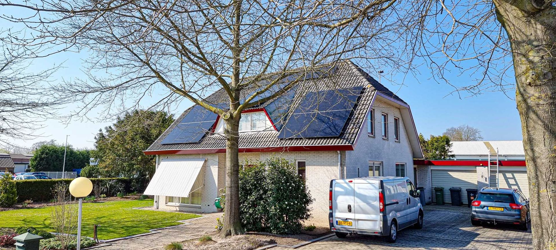 Een wit huis met zonnepanelen op het dak en een wit busje ervoor geparkeerd.