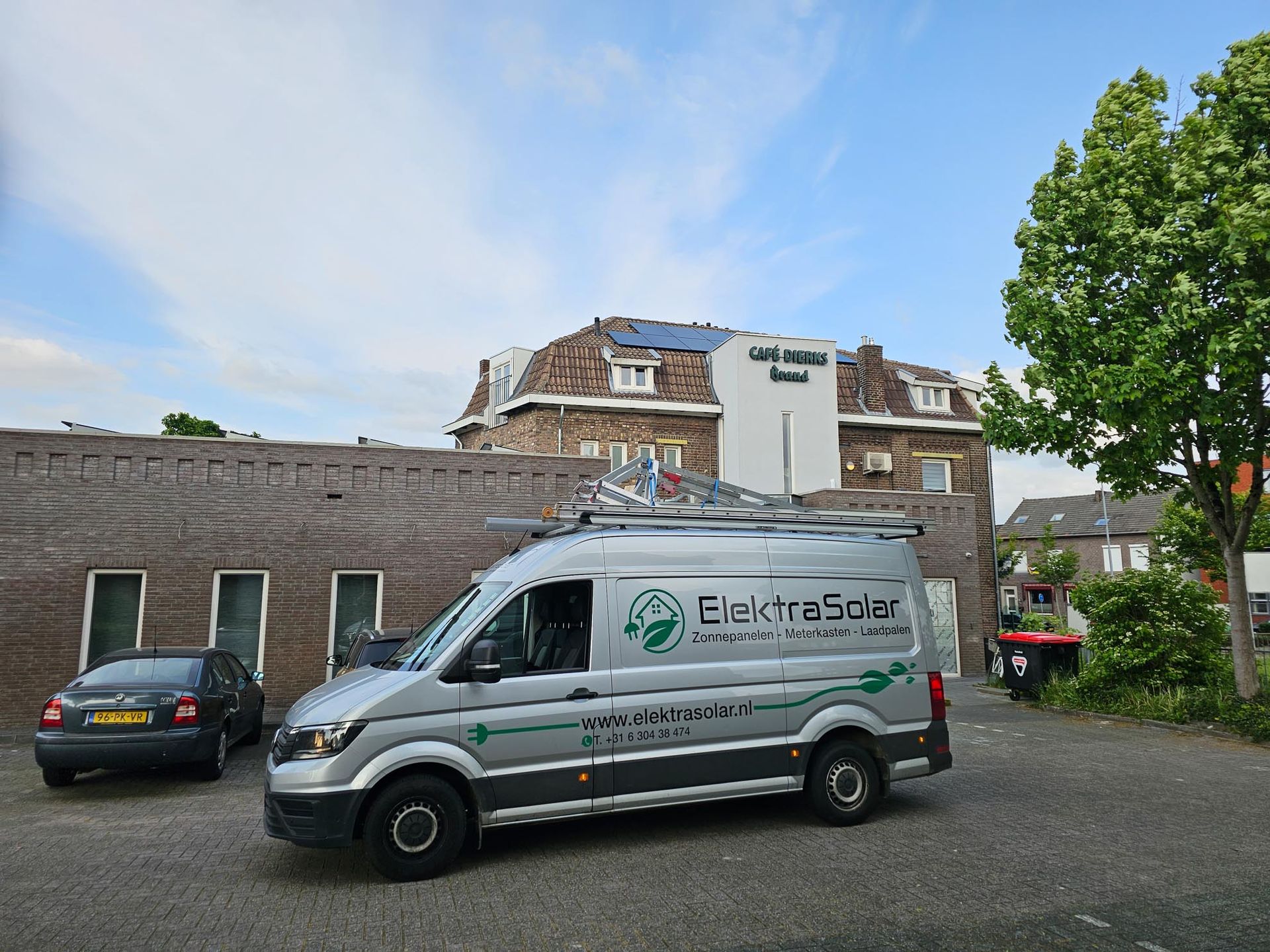 Een busje staat geparkeerd voor een gebouw met zonnepanelen op het dak.
