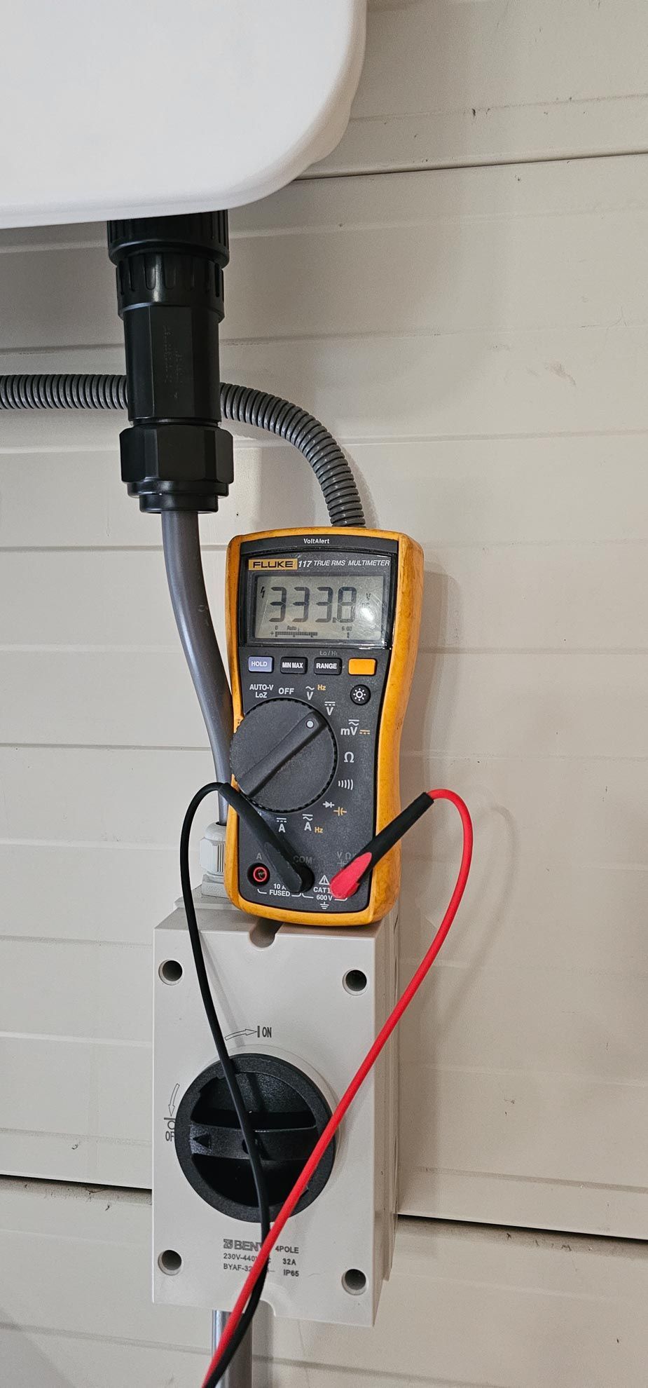 Een multimeter wordt in een stopcontact in de muur gestoken.