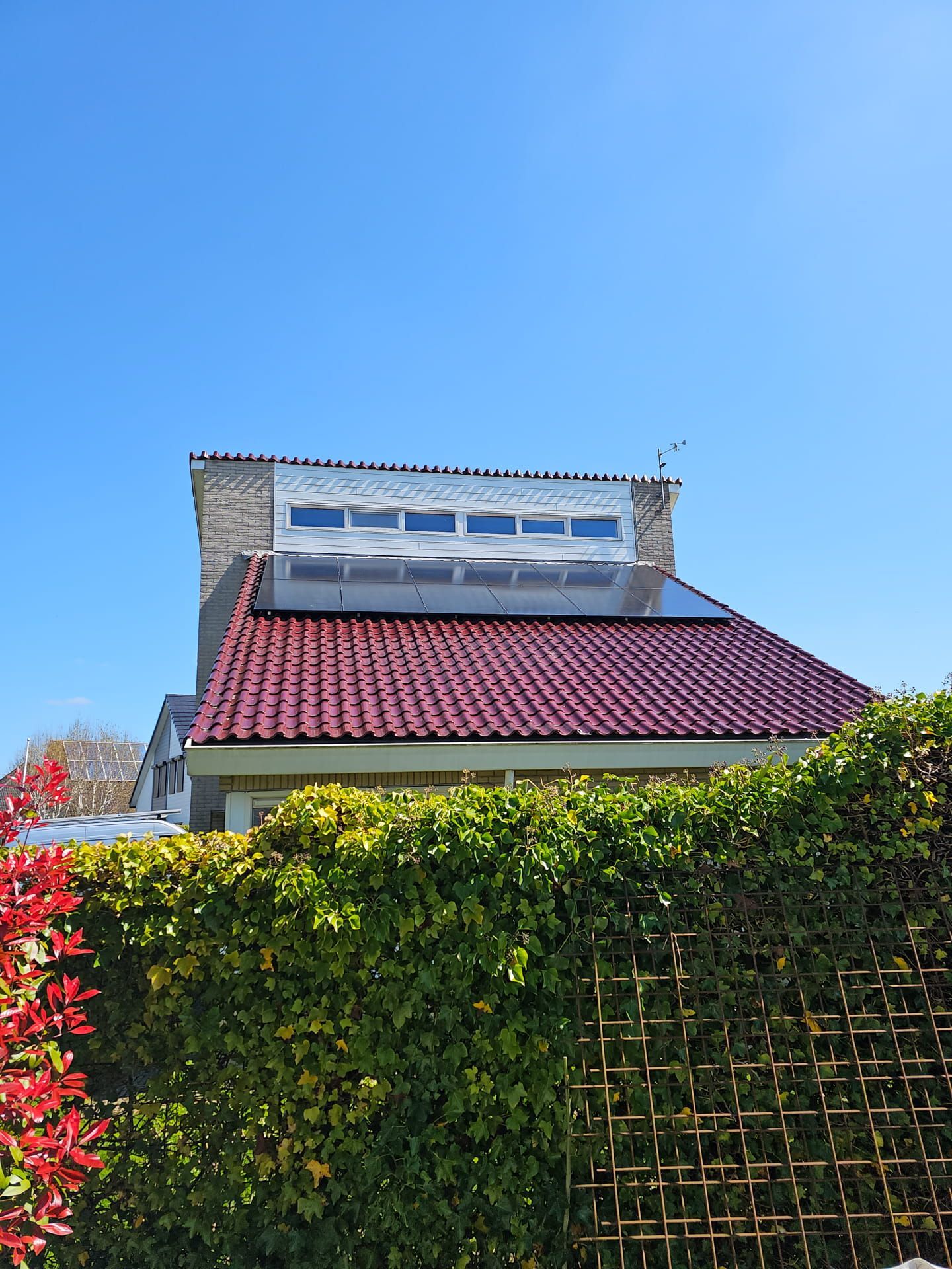 Een huis met een rood pannendak en een zonnepaneel op het dak.