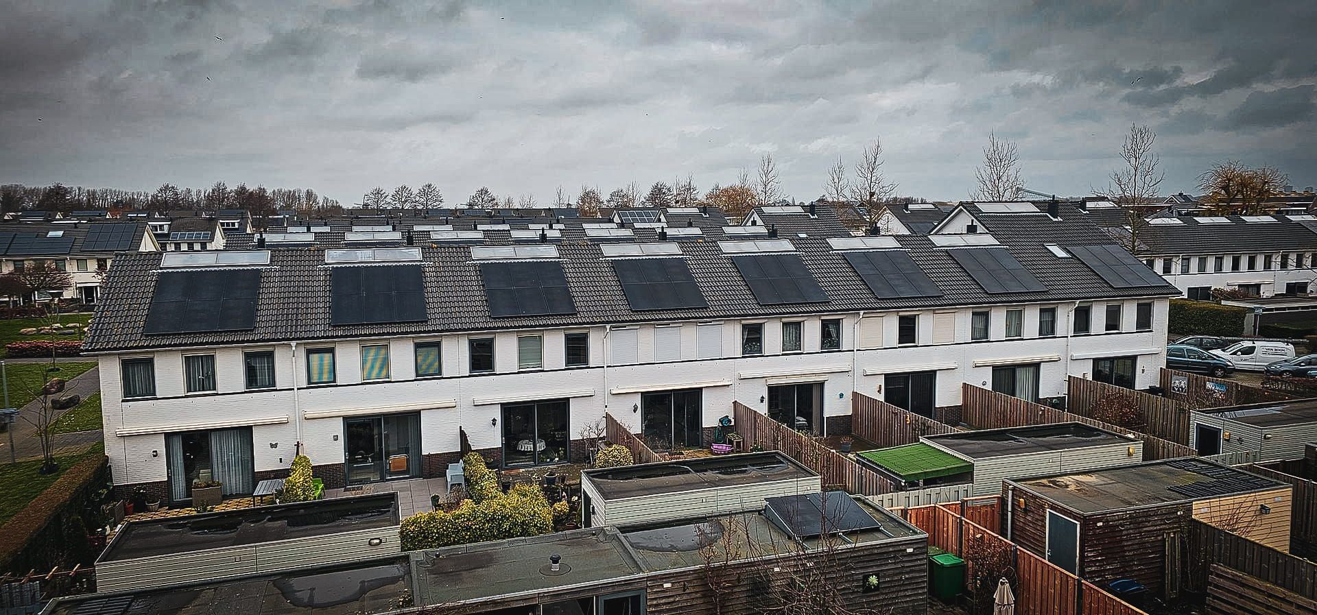 Een luchtfoto van een rij huizen met zonnepanelen op de daken.