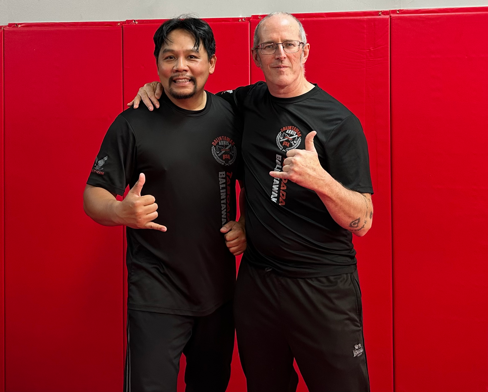 Two men are posing for a picture in front of a red wall.