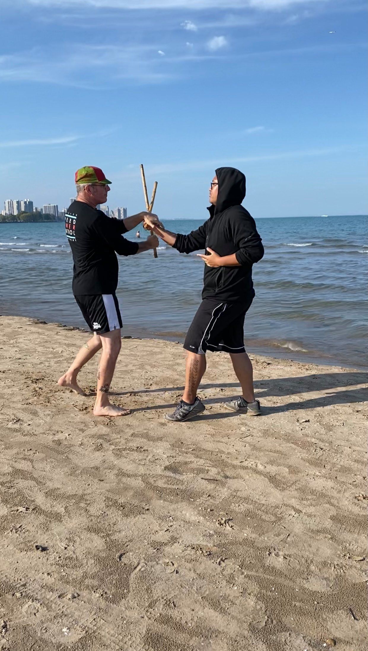 Two men are standing on a beach holding sticks.