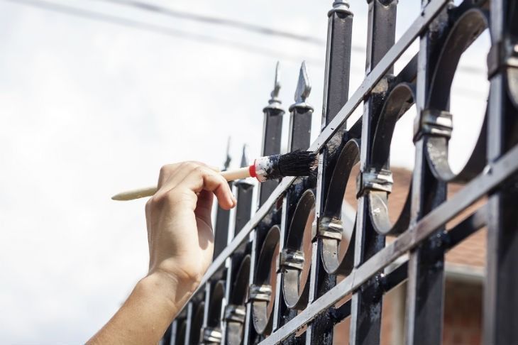 A person is painting a wrought iron fence with a brush.