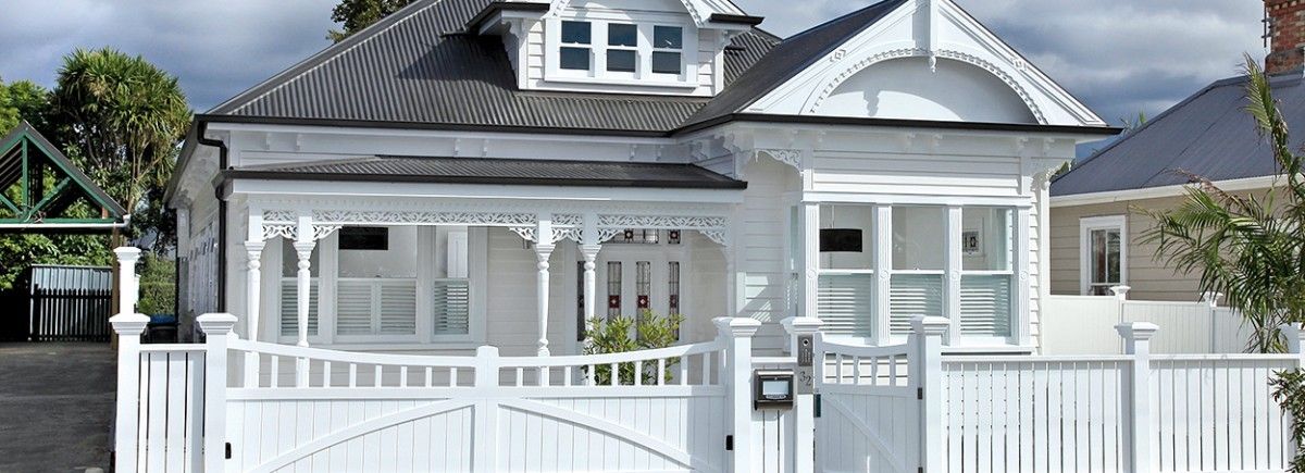 A white house with a black roof and a white fence.