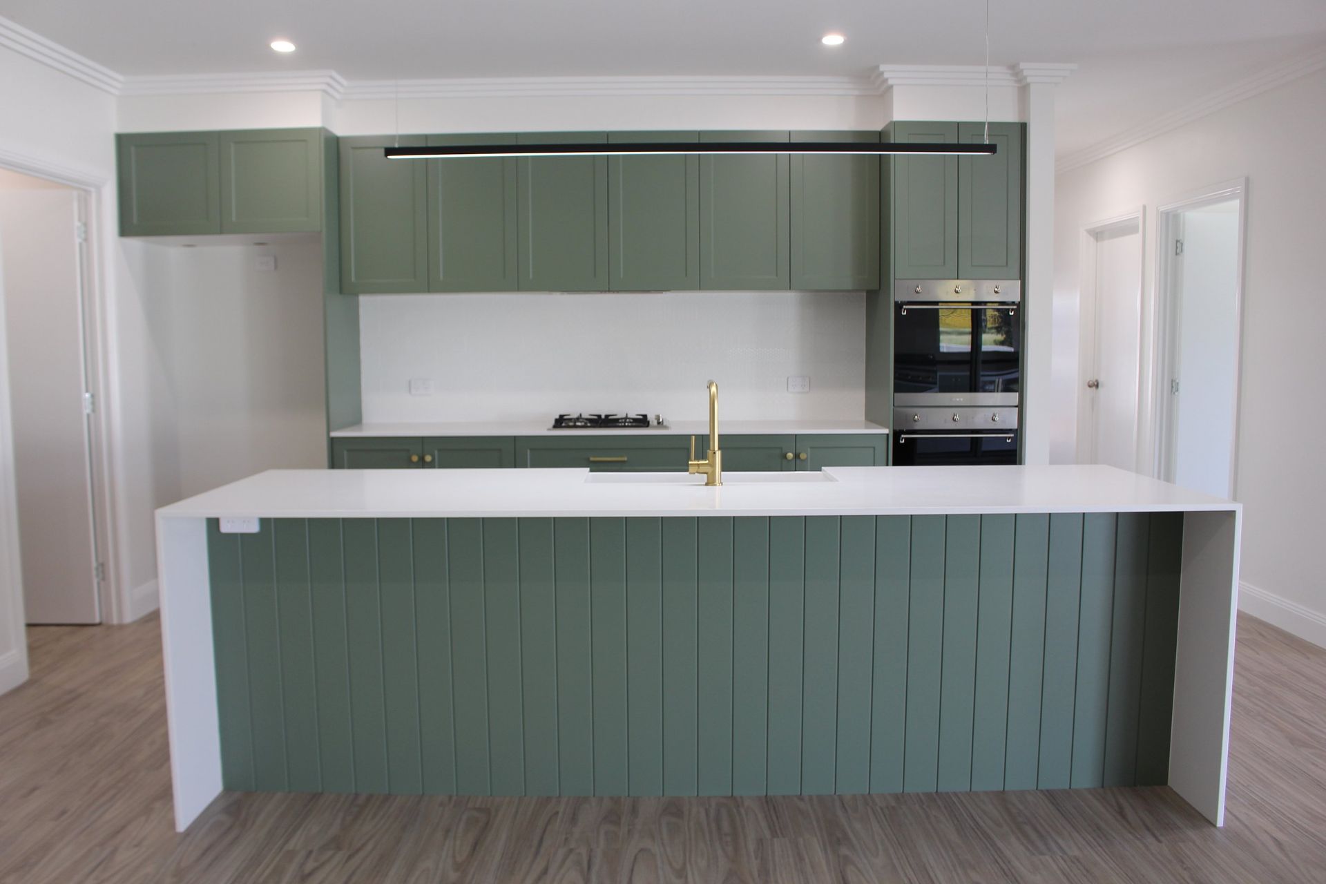 A kitchen with green cabinets , white counter tops , and a large island.