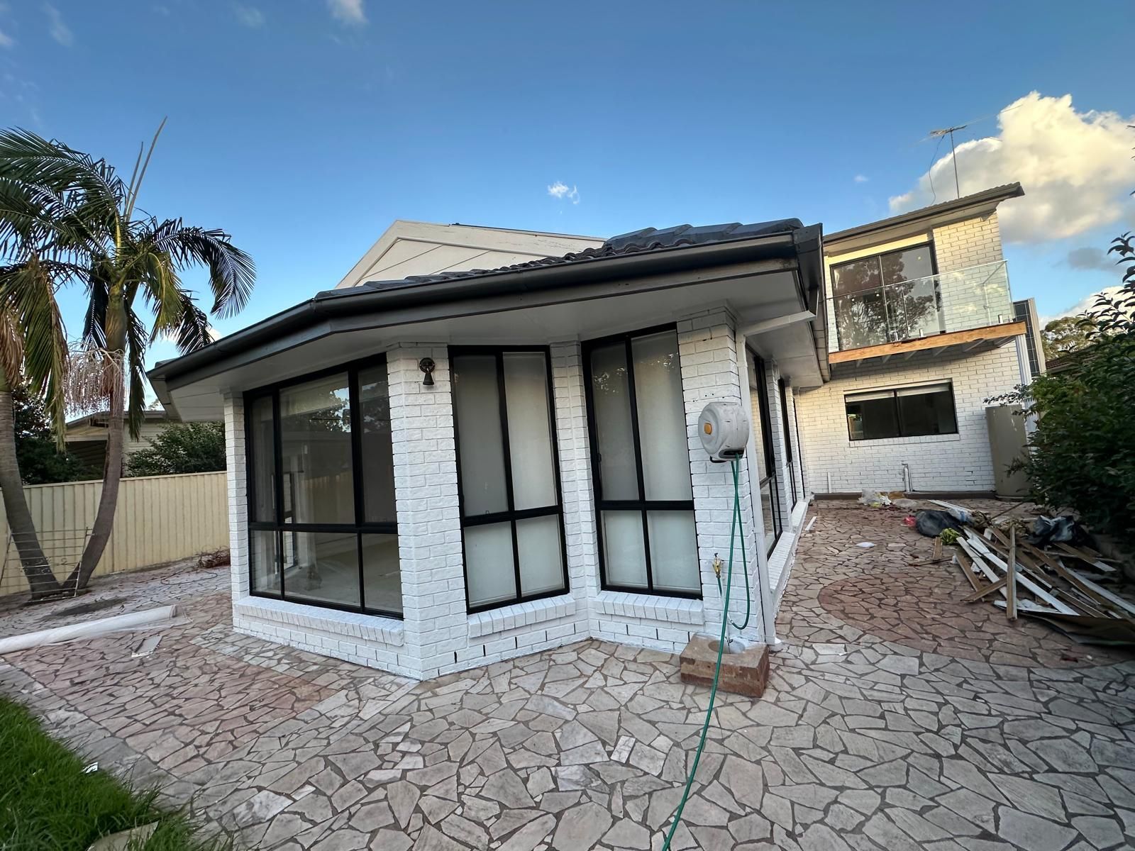 A white brick house with black windows and a hose in front of it.