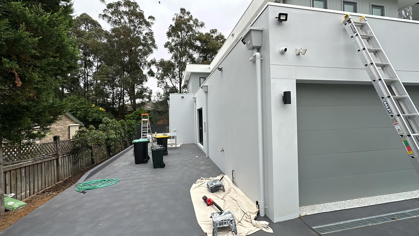 A white house is being painted with a ladder on the side of it.