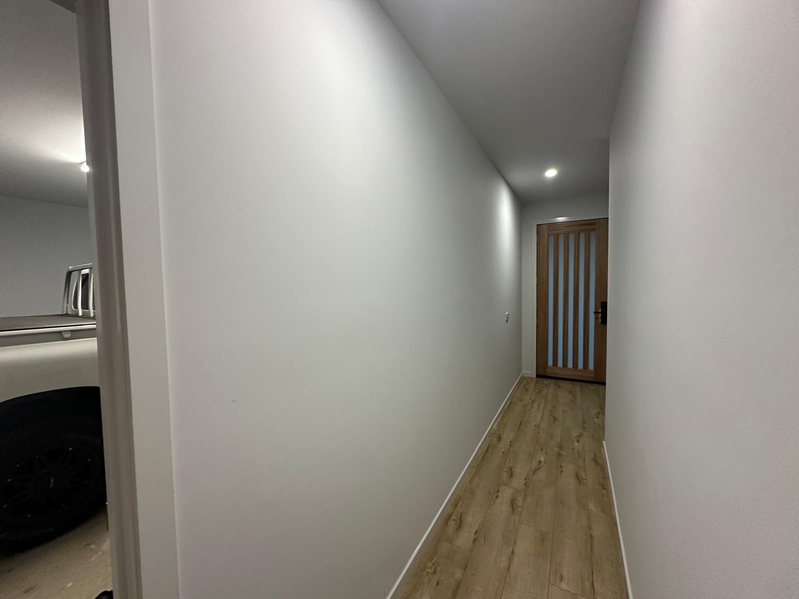 A long hallway with white walls and wooden floors leading to a bathroom.